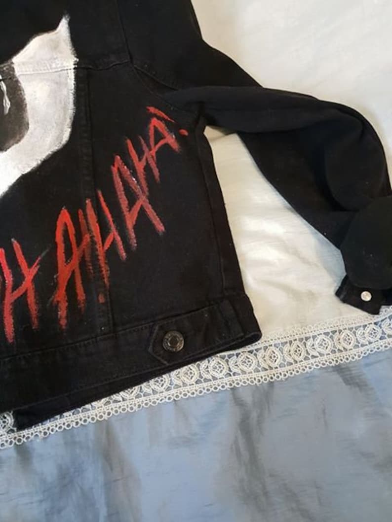 Op de afbeelding: Zwart denim jack met witte verf en rode letters die "HAHAHA" zeggen.