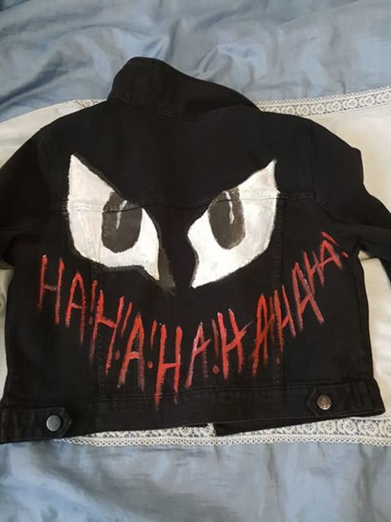Op de afbeelding: Een zwart denim jack met een wit en zwart geschilderd Joker-gezicht en de woorden "HAHAHA" in rode verf.
