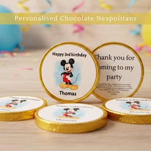 May include: Chocolate Neapolitans with gold foil wrappers. The candies feature a Mickey Mouse design with the text "Happy 3rd birthday" and "Thomas". One candy says "Thank you for coming to my party". Party decorations are in the background.