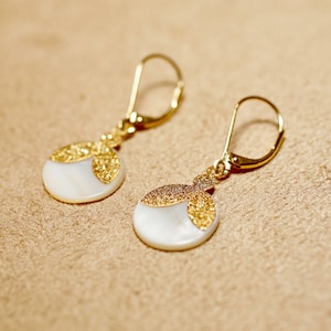 May include: A pair of gold earrings with white shell and gold accents. The earrings have a simple, elegant design.