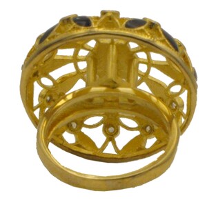 May include: A gold ring with a filigree design and black enamel accents. The ring is set with small clear stones.