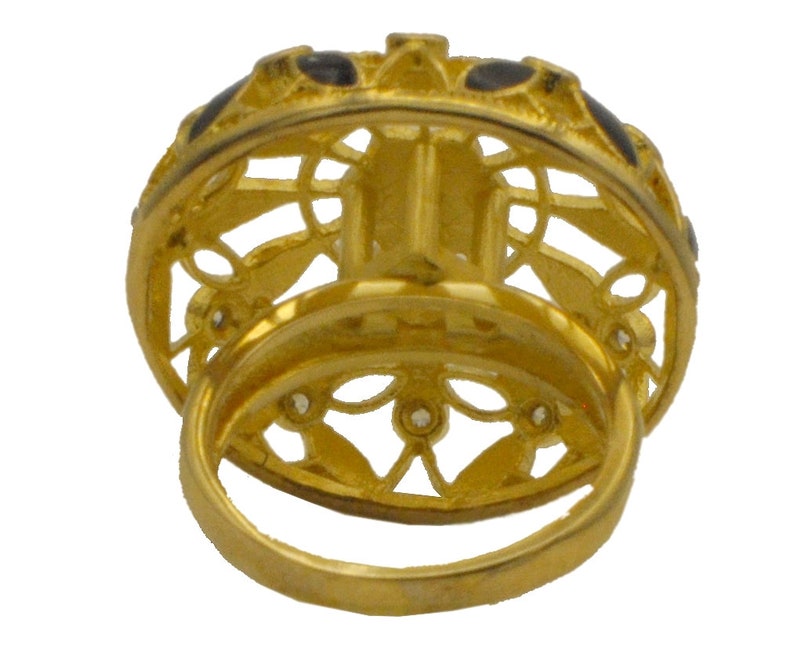 May include: A gold ring with a filigree design and black enamel accents. The ring is set with small clear stones.