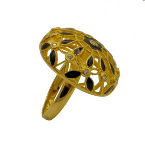 May include: A gold ring featuring a black enamel design and clear stones. The ring has a floral pattern and is set against a white background.