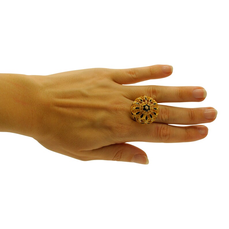 May include: A gold ring featuring a round, intricate design. The ring is decorated with black enamel and a small, clear stone in the centre.