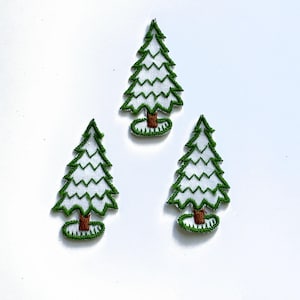 May include: Three embroidered Christmas tree patches. Each tree features a white body with green zigzag edges, a brown trunk, and a green base. The patches are set against a white background.