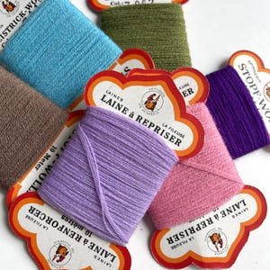 May include: Assortment of colourful yarn spools with labels in French. The labels read "La Fileuse" and "Laine &agrave; Repriser".