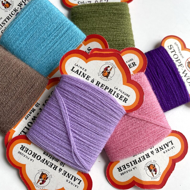 May include: Assortment of colourful yarn spools with labels in French. The labels read "La Fileuse" and "Laine &agrave; Repriser".