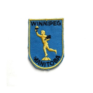 May include: A blue and yellow embroidered patch with the text "WINNIPEG MANITOBA" and a gold figure holding a torch.