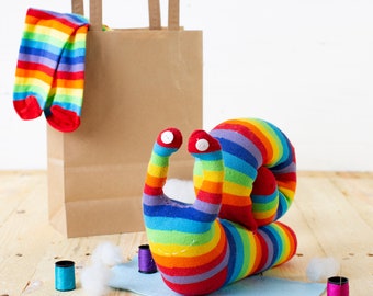 May include: A rainbow striped sock snail with googly eyes. The snail is made from a pair of rainbow striped socks and is sitting on a blue surface. There are some colorful buttons and spools of thread nearby.