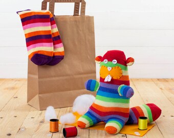 May include: A rainbow striped sock puppet in the shape of a beaver with a brown paper bag and a pair of striped socks in the background.