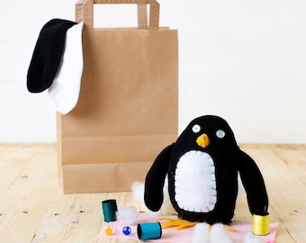 May include: A brown paper bag with a black and white penguin toy, sewing supplies, and a pink piece of fabric.