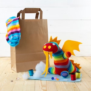 May include: A rainbow striped sock dragon toy with yellow felt horns and a brown paper bag with a rainbow striped sock sticking out of the top.