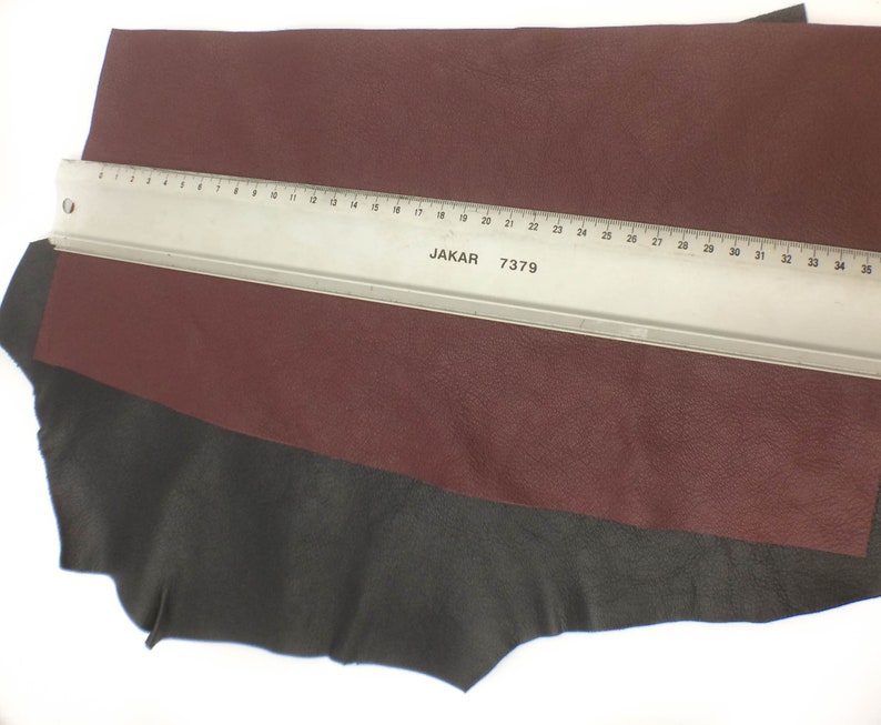 May include: A piece of burgundy leather with a black leather border. A ruler with the text "JAKAR 7379" is placed on top of the leather.