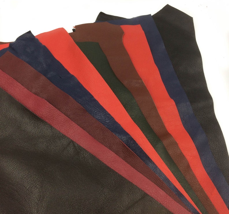 May include: Assortment of leather strips in various colors, including black, dark brown, burgundy, red, navy blue, and green. The leather is textured and appears to be of high quality.
