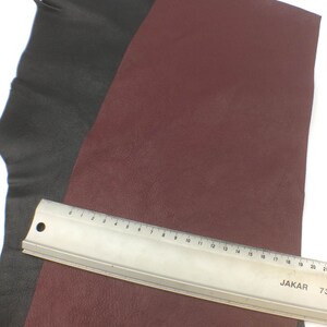 May include: Two pieces of leather, one black and one burgundy, are laid out on a white surface. A metal ruler with markings in inches is placed on top of the burgundy leather.