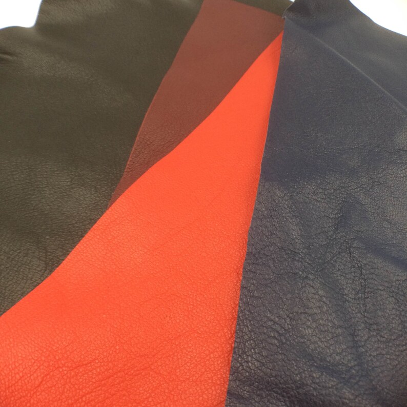 May include: Four pieces of leather in different colors: black, burgundy, red, and navy blue. The leather is textured and has a natural grain.