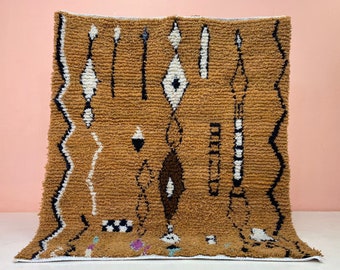 May include: A brown, white, and black patterned rug with a geometric design. The rug has a fringe border.