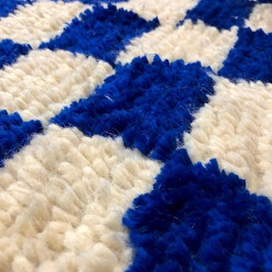 Peut inclure: Gros plan sur un tapis blanc et bleu avec un motif g&eacute;om&eacute;trique. Le tapis est fait de fils moelleux et textur&eacute;s.