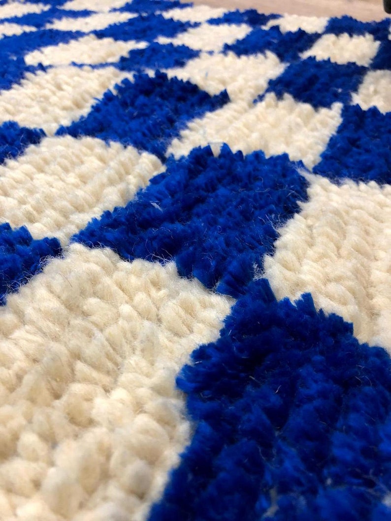 Peut inclure: Gros plan sur un tapis blanc et bleu avec un motif g&eacute;om&eacute;trique. Le tapis est fait de fils moelleux et textur&eacute;s.