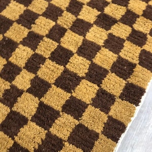 K&ouml;nnte beinhalten: Ein brauner und goldener karierter Teppich mit einem wei&szlig;en Fransenrand.