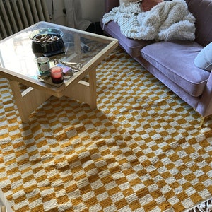 May include: A yellow and white checkered rug with a wooden coffee table and a purple sofa in the background.