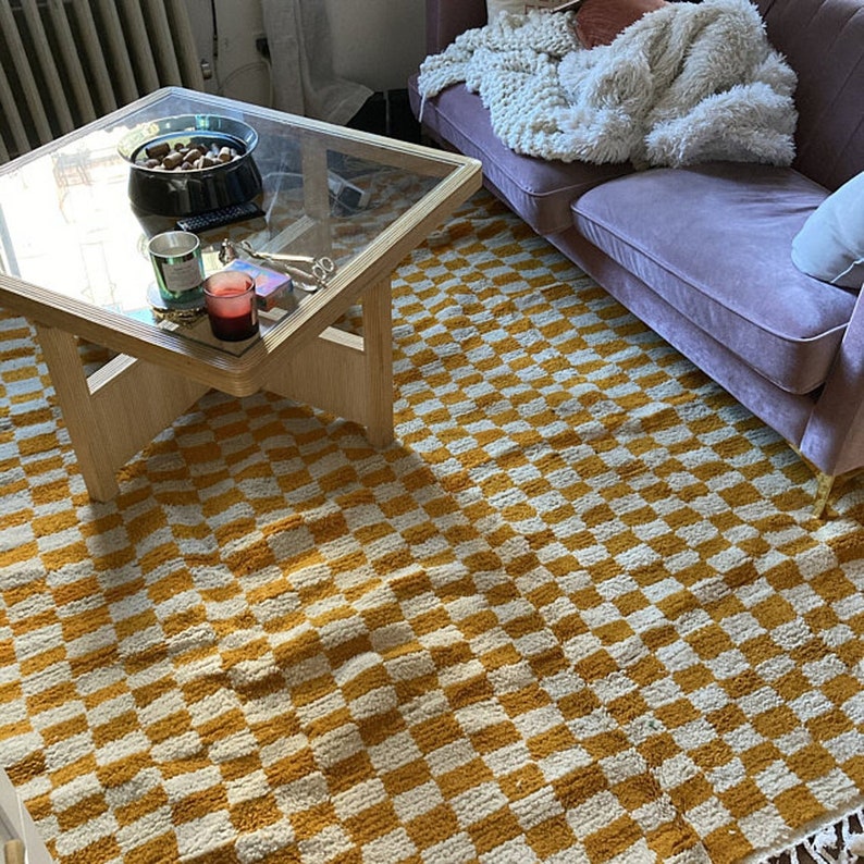 May include: A yellow and white checkered rug with a wooden coffee table and a purple sofa in the background.