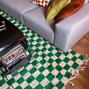 May include: A gray sofa with pillows and a green and white checkered rug. The rug has a fringe border. There is a black coffee table with a stack of records on it.