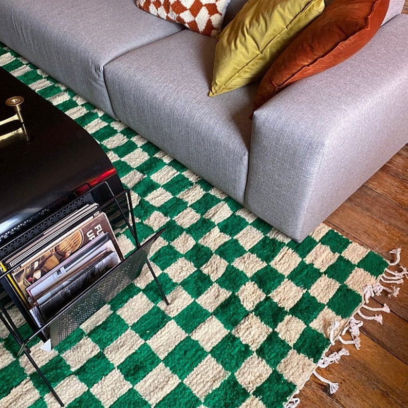 May include: A gray sofa with pillows and a green and white checkered rug. The rug has a fringe border. There is a black coffee table with a stack of records on it.