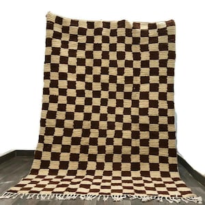 May include: A brown and cream checkered rug with fringe on the edges. The rug is made of wool and has a soft, textured feel.