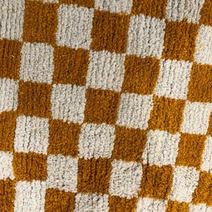 May include: A checkered rug with alternating squares of white and mustard yellow. The rug is made of a soft, fluffy material.