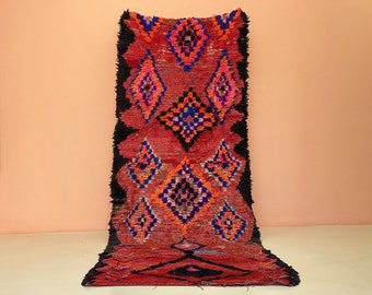 May include: A red, black, blue, and orange Moroccan rug with a diamond pattern.