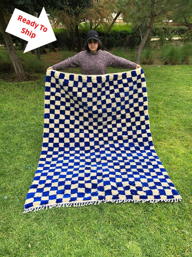 May include: A large blue and white checkered rug with fringe. The rug is made of wool and has a soft, plush texture.
