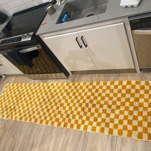Peut inclure: Un long tapis rectangulaire &agrave; carreaux avec un motif jaune et blanc. Le tapis a des franges aux deux extr&eacute;mit&eacute;s.