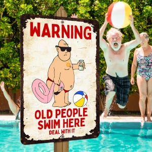 May include: A weathered metal sign with the text "WARNING OLD PEOPLE SWIM HERE DEAL WITH IT" features a cartoon of a man in sunglasses holding a beer and a flamingo float. A beach ball and people in a pool are in the background.