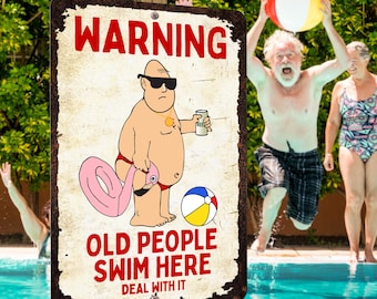 Op de afbeelding: Een verweerd metalen bord met de tekst "WARNING OLD PEOPLE SWIM HERE DEAL WITH IT" toont een cartoon van een man met een zonnebril die een biertje en een flamingo-drijver vasthoudt. Een strandbal en mensen in een zwembad zijn op de achtergrond.