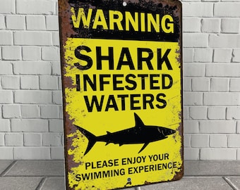 May include: A yellow and black warning sign with the text "WARNING SHARK INFESTED WATERS" and a silhouette of a shark. The sign also says "PLEASE ENJOY YOUR SWIMMING EXPERIENCE".