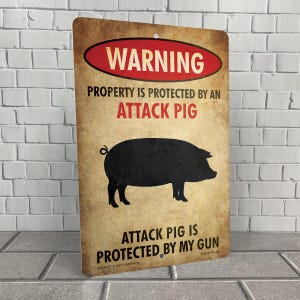 May include: A warning sign with a distressed, aged look. The sign is brown with red and black text. It reads "WARNING PROPERTY IS PROTECTED BY AN ATTACK PIG ATTACK PIG IS PROTECTED BY MY GUN". A black silhouette of a pig is in the center of the sign.