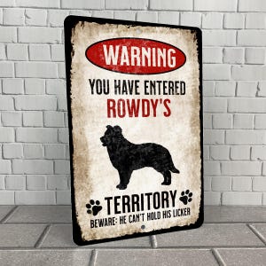 May include: A warning sign with a black silhouette of a dog and the text "Warning You Have Entered Rowdy's Territory Beware: He Can't Hold His Licker"
