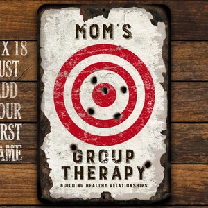 May include: A white metal sign with a red and white target in the center. The sign says "Mom's Group Therapy Building Healthy Relationships".