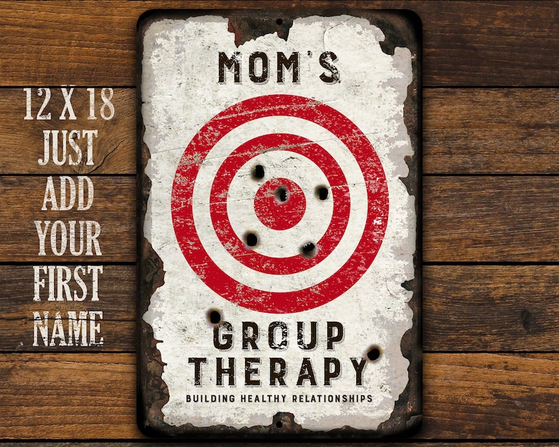 May include: A white metal sign with a red and white target in the center. The sign says "Mom's Group Therapy Building Healthy Relationships".
