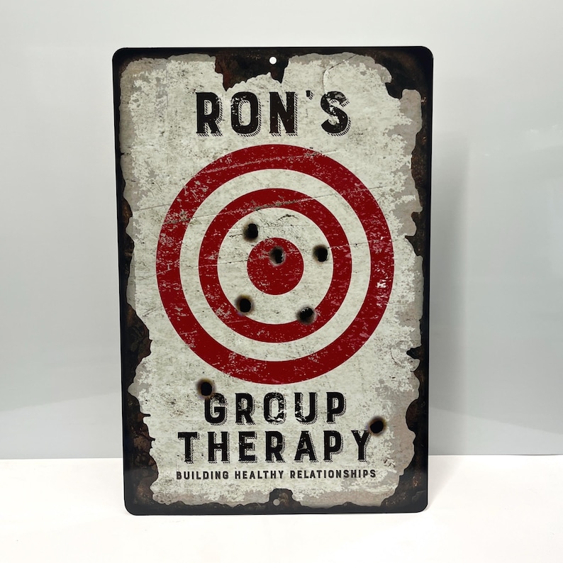 May include: A white metal sign with a red and white target with bullet holes. The sign reads "Ron's Group Therapy Building Healthy Relationships".