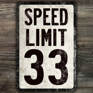 May include: A vintage-style speed limit sign with a white background and black text. The sign reads "SPEED LIMIT 33".
