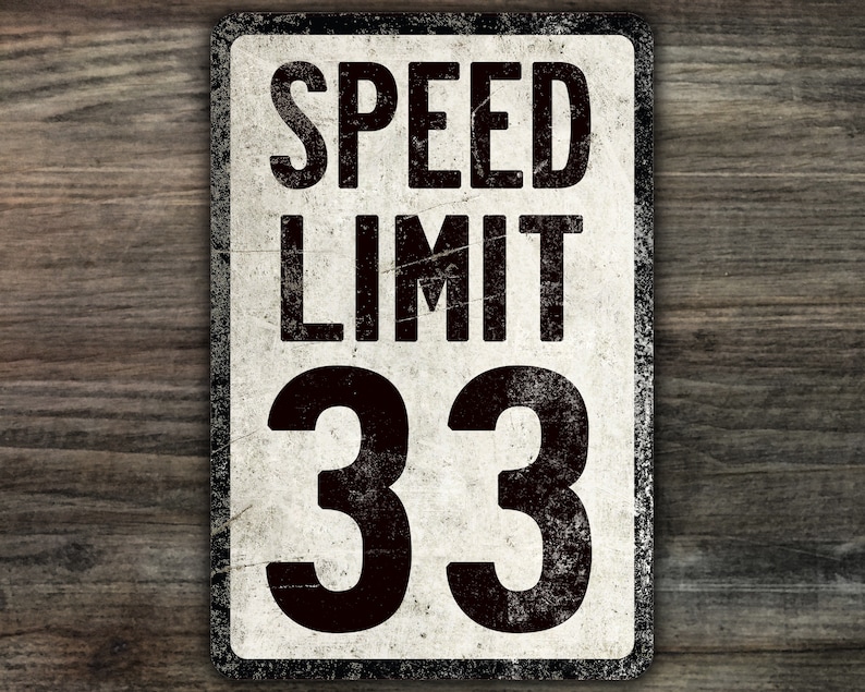 May include: A vintage-style speed limit sign with a white background and black text. The sign reads "SPEED LIMIT 33".