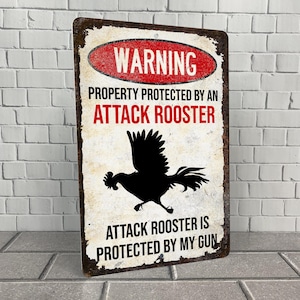 May include: A white metal sign with a red warning sign that says "WARNING PROPERTY PROTECTED BY AN ATTACK ROOSTER ATTACK ROOSTER IS PROTECTED BY MY GUN". The sign features a black silhouette of a rooster.