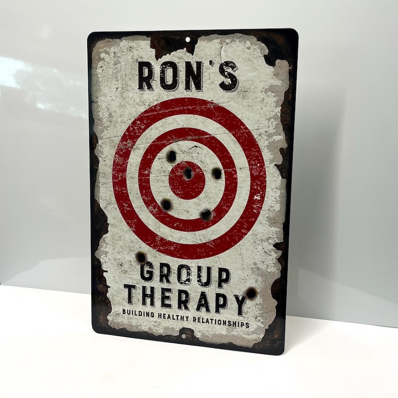 May include: A vintage-style metal sign with a red and white target with bullet holes. The sign reads "Ron's Group Therapy Building Healthy Relationships".