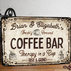 May include: A vintage-style sign with a brown background and black lettering. The sign reads "Brian & Elizabeth's Freshly Brewed Coffee Bar Therapy in a Cup - Rise & Grind -" with a coffee cup and grinder illustration.
