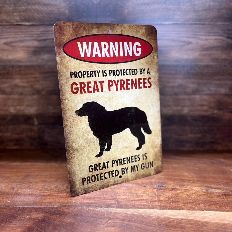 Puede incluir: Un cartel de advertencia con un aspecto desgastado y vintage. El cartel dice "WARNING PROPERTY IS PROTECTED BY A GREAT PYRENEES GREAT PYRENEES IS PROTECTED BY MY GUN". Una silueta negra de un perro de monta&ntilde;a de los Pirineos aparece en el cartel.