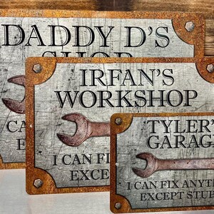 Puede incluir: Tres letreros met&aacute;licos con un acabado envejecido. Los letreros dicen "Daddy D's Shop", "Irfan's Workshop" y "Tyler's Garage". Cada letrero presenta un gr&aacute;fico de llave inglesa y la frase "I can fix anything except stupid".
