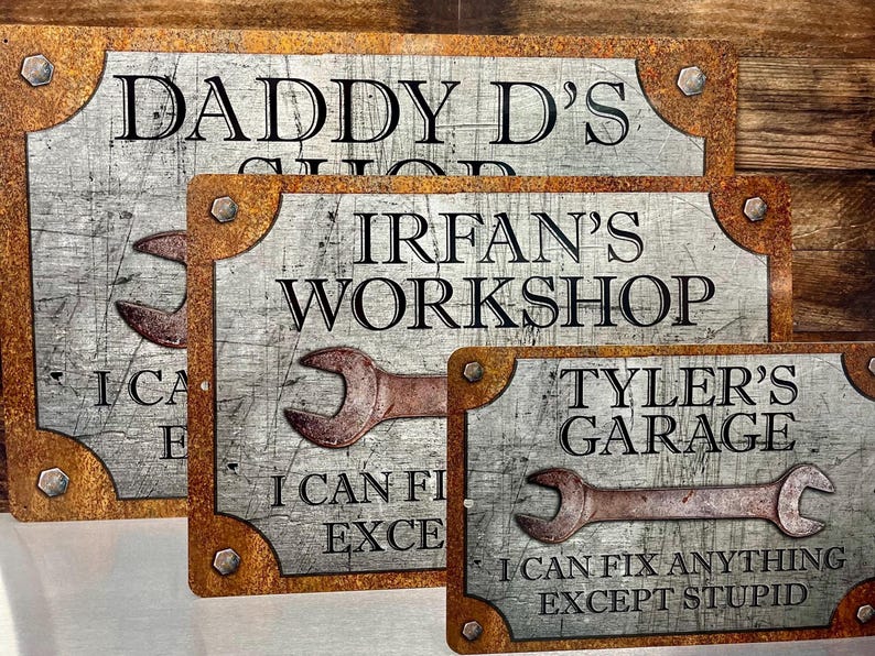 Puede incluir: Tres letreros met&aacute;licos con un acabado envejecido. Los letreros dicen "Daddy D's Shop", "Irfan's Workshop" y "Tyler's Garage". Cada letrero presenta un gr&aacute;fico de llave inglesa y la frase "I can fix anything except stupid".