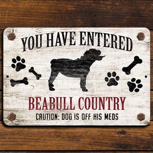 May include: White wooden sign with black text that reads "You Have Entered Beabull Country. Caution: Dog is off his meds."  The sign features a black silhouette of a bulldog and paw prints.